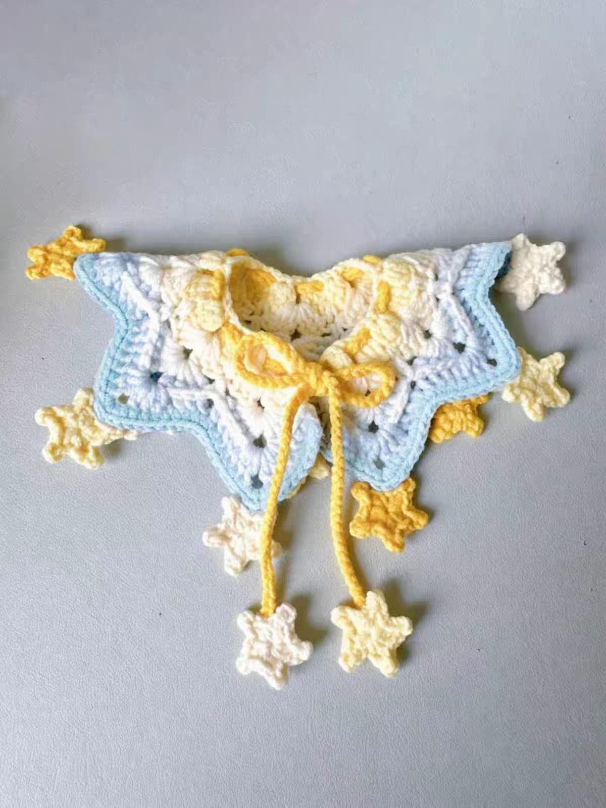 Soft handmade crochet cat scarf accessory laid out with flower and star charm details